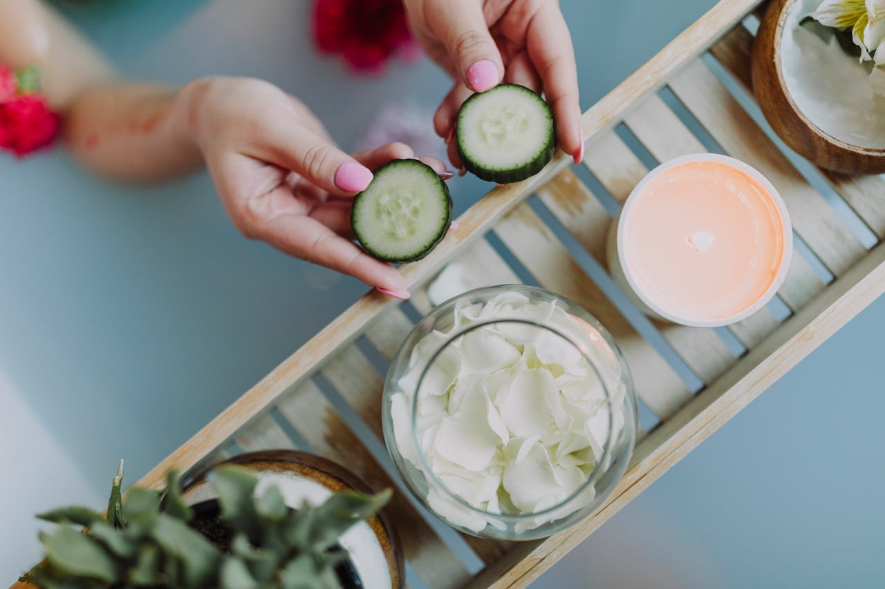 Top view of spa essentials including cucumber slices, candles, and petals.