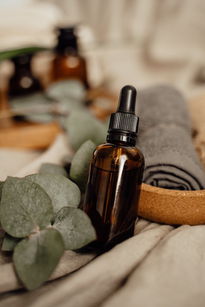 Relaxing spa setup featuring an amber dropper bottle, eucalyptus leaves, and towel.